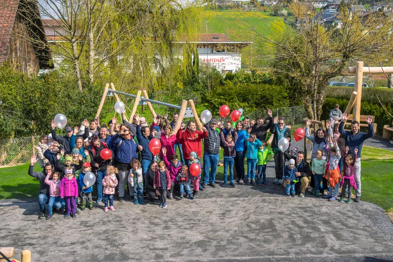 Grosses Gruppenfoto am Eröffnungsfest: Dutzende Dorfbewohner aller Generationen stehen vor den Holz-Spielgeräten des Generationenparks.
